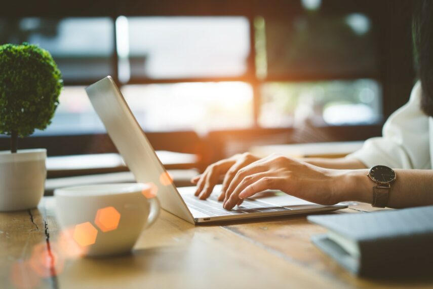 man in front of table typing on laptop with a sunrise in the background 